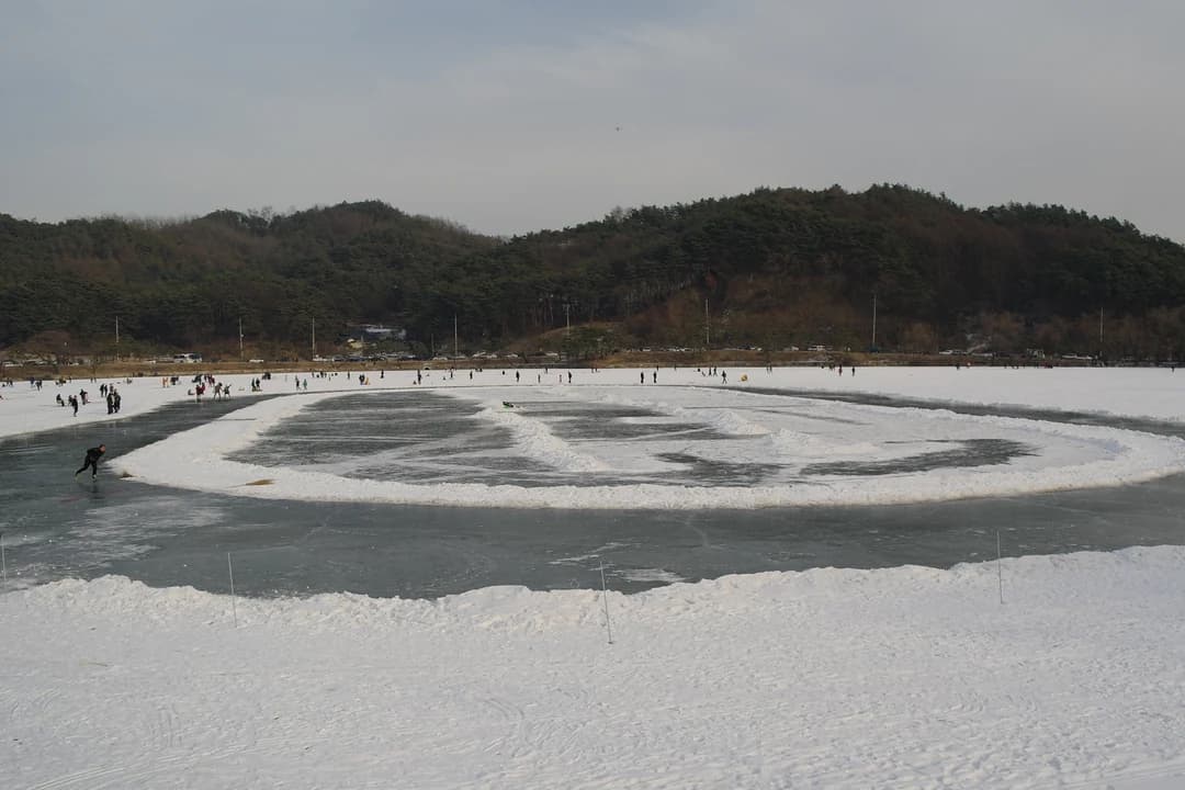 A frozen lake with a cleared ice rink, visitors in the distance and wooded hills behind
