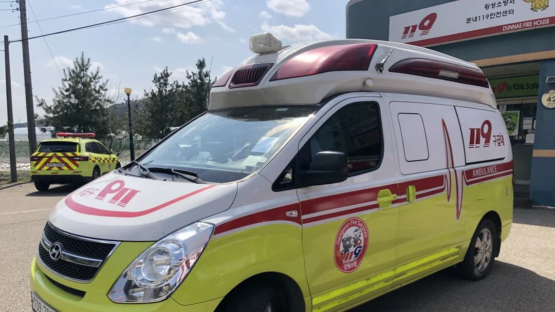 A yellow-green and white 119 ambulance parked outside a fire station