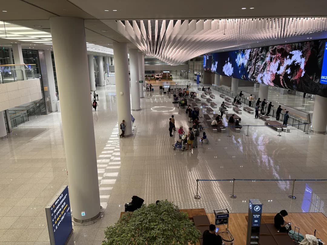 A tall arrivals and departures hall at Incheon Airport with large columns and a big display screen